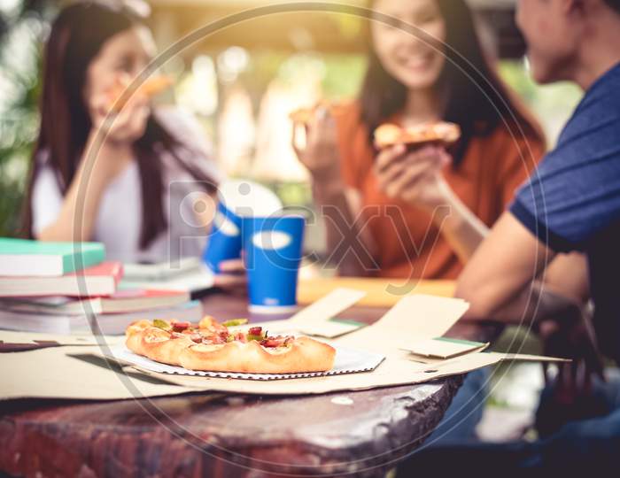 Three Asian People Enjoy Eating Pizza At Outdoors After Tutoring Class. Education And Party Concept. Food And Drinks Theme. Happiness Lifestyle Theme.