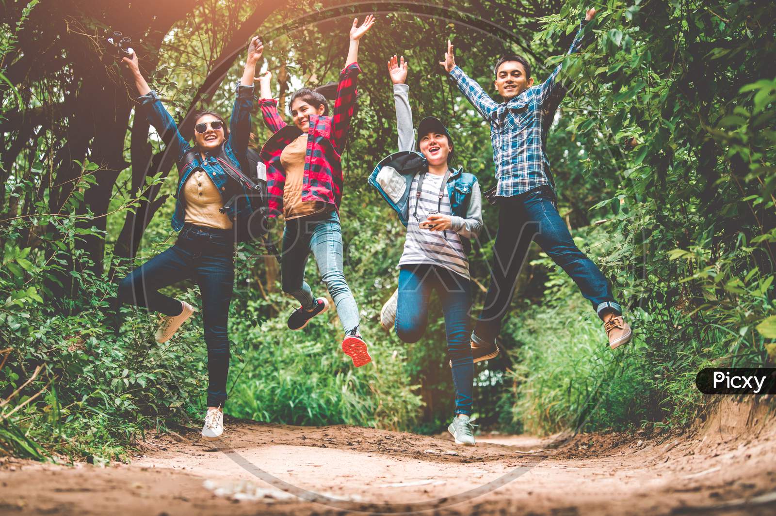 Group Of Happy Asian Teenage Adventure Traveler Trekkers Group Jumping Together In Mountain At Outdoor Forest Background. Young Hiker Friends Supporting Each Others As Survival Team Travel And Success