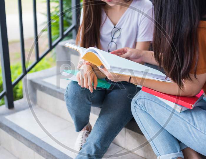 Close Up Of Two Asian Beauty Girls Reading And Tutoring Books For Final Examination Together. Student Smiling And Sitting On Stair. Education And Back To School Concept. Lifestyles And People Theme.