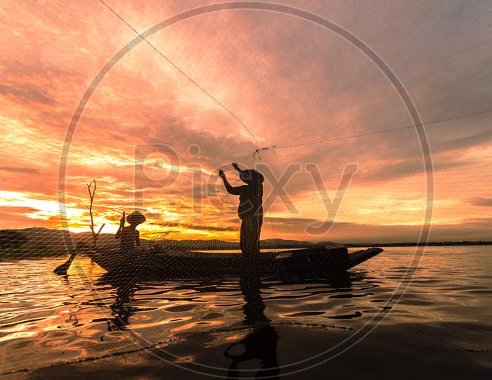 Silhouette Fisherman Fishing By Using Net On The Boat In Morning In Thailand, Nature And Culture Concept