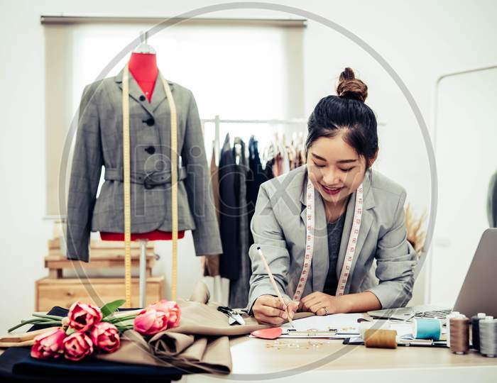 Attractive Asian Female Fashion Designer  Working In Home Office Workshop. Stylish Fashionista Woman Creating New Cloth Design Collection. Tailor And Sewing. People Lifestyle And Occupation Concept