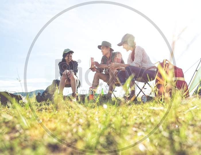 Group Of Travelers Camping And Doing Picnic In Meadow Field Foreground. Mountain And Lake Background. People And Lifestyles Concept. Outdoors Activity And Leisure Theme. Backpacker And Hiker Theme