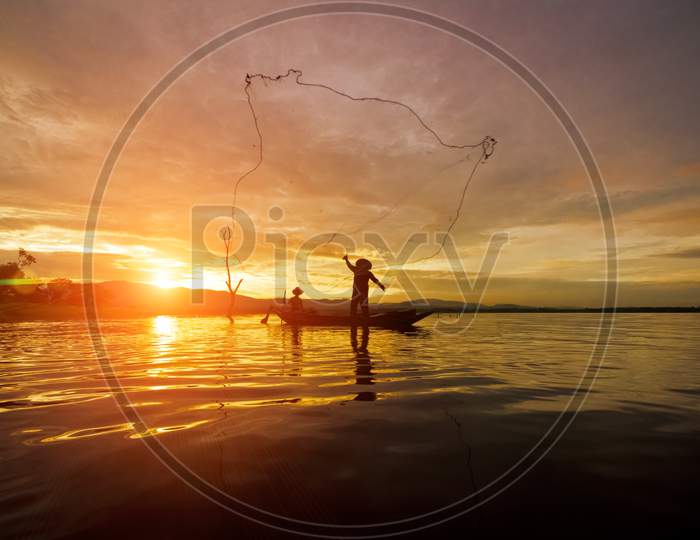 Silhouette Fisherman Fishing By Using Net On The Boat With Sunshine In Thailand In The Morning ,Nature And Culture Concept