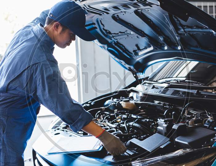 Car Mechanic Checking To Maintenance Vehicle By Customer Claim Order In Auto Repair Shop Garage By List In Clipboard. Engine Repair Service. People Occupation And Business Job. Automobile Technician