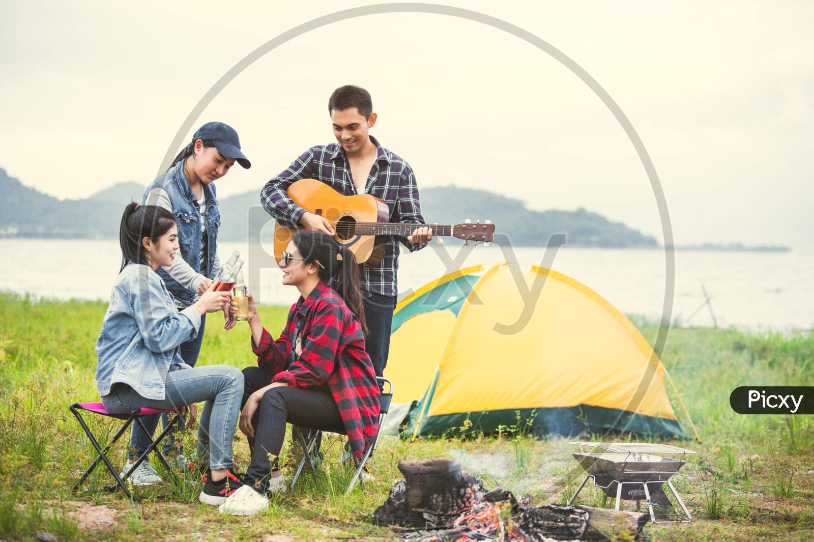 Group Of Asian Friendship Clinking Drinking Bottle Glass For Celebrating In Private Party With Mountain And Lake View Background. People Lifestyle Travel On Vacation Concept. Picnic And Camping Tent