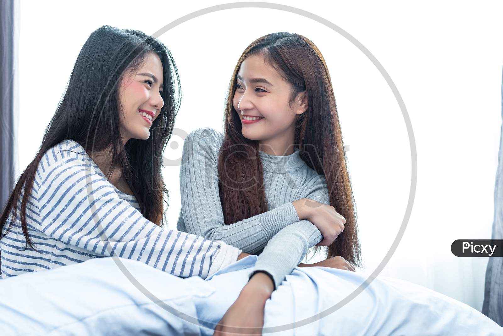Two Asian Lesbian Women Looking Together In Bedroom. Couple People And Beauty Concept. Happy Lifestyles And Home Sweet Home Theme. Cushion Pillow Element And Window Background.