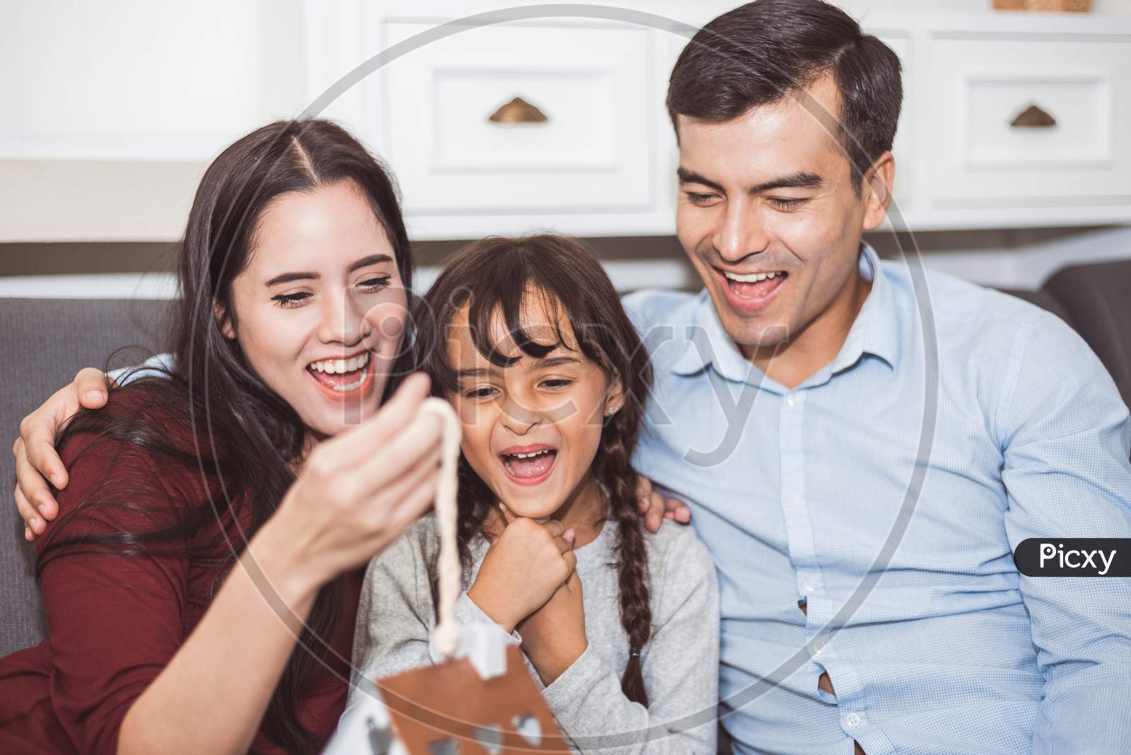 Father And Mother Surprise Their Daughter By Gift Or New Toy. Parents And Children Are Happy Together In Home On Sofa In Living Room. Family And Happiness Of Life Concept.