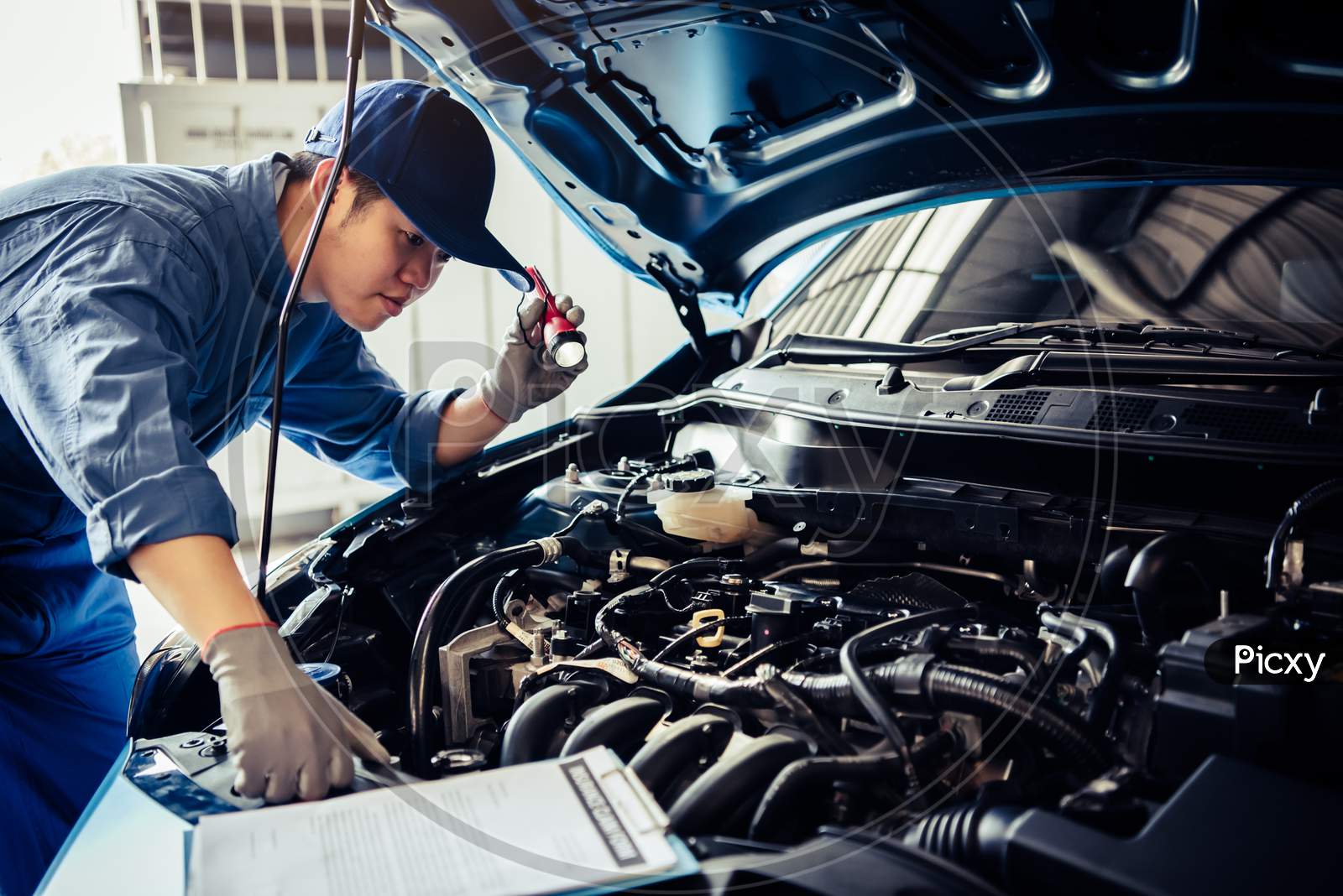 Car Mechanic Technician Holding Flashlight Checking Engine With Checklist Clipboard To Maintenance Vehicle By Customer Claim Order In Auto Repair Shop Garage Repair Service. People Occupation Business