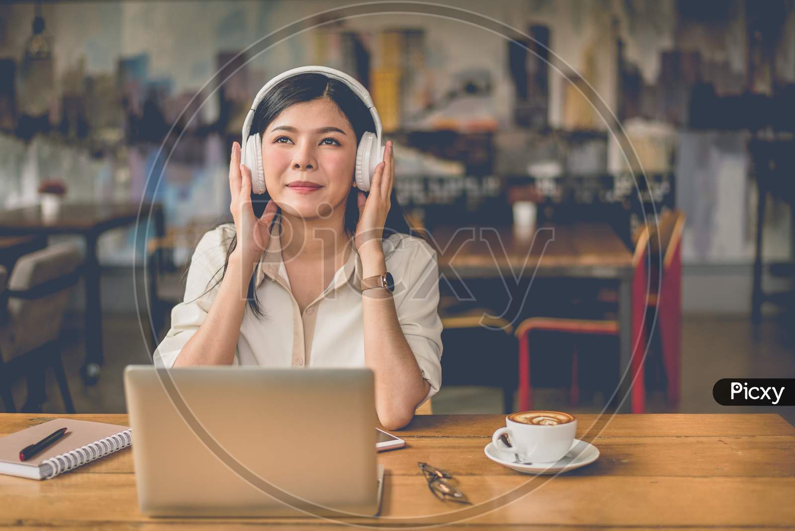 Happy Asian Woman Relaxing And Listening Music In Coffee Shop With Computer Laptop And Coffee Cup. People And Lifestyles Concept. Freelance And Outdoors Workplace Outdoors Theme.
