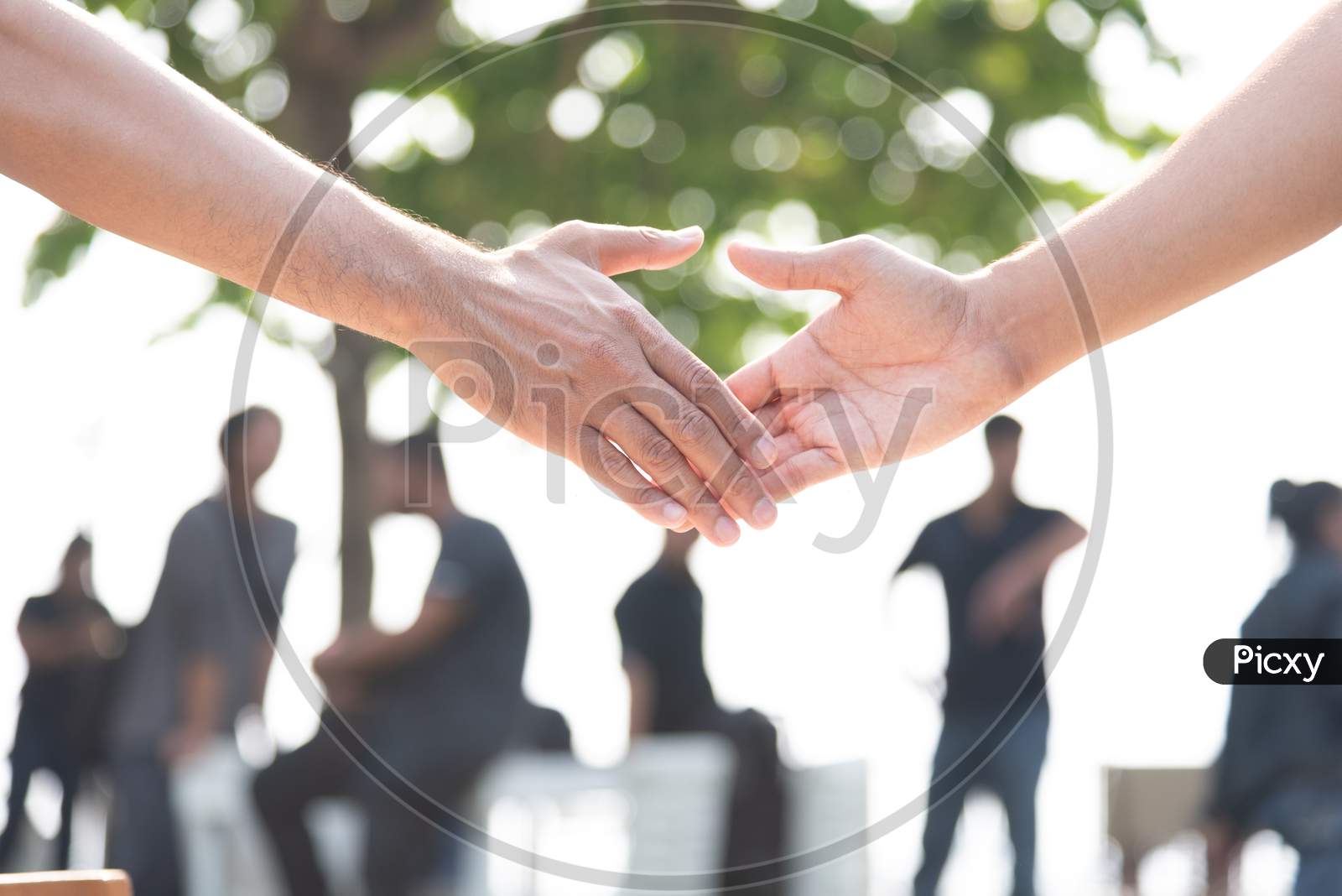 Closed Up Of Hand Shake With People In Background. Business Cooperation And Unity Concept. Business And Outdoors Theme.