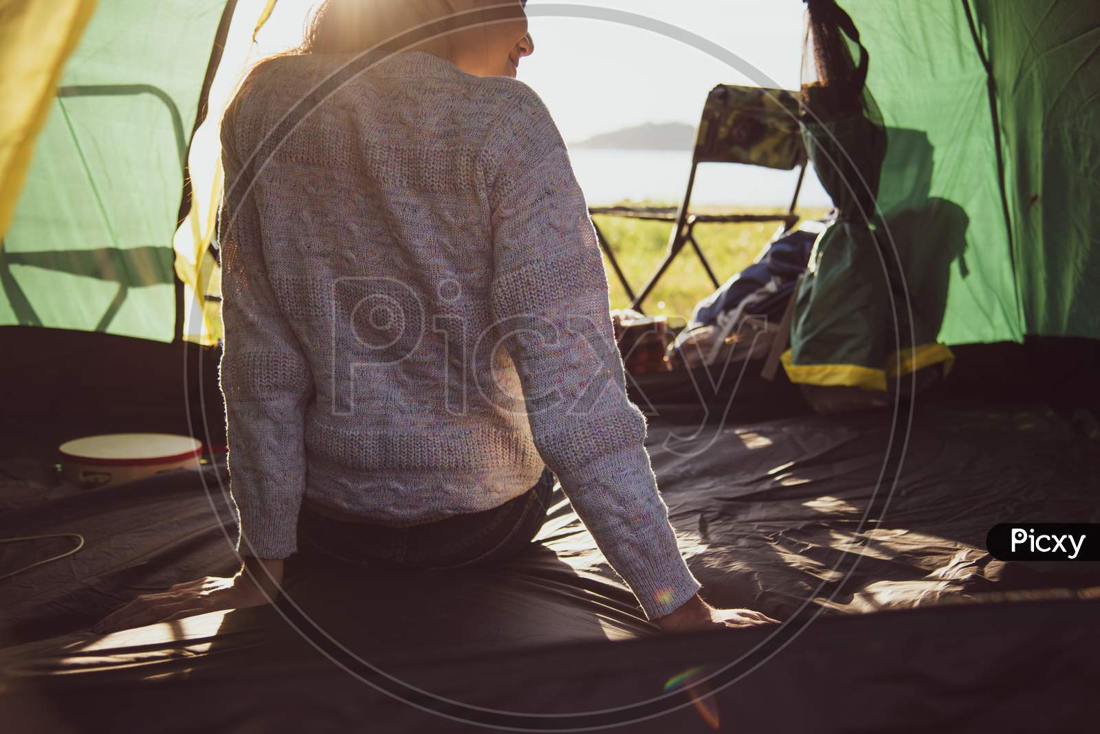 Back View Of Happy Female Tourist Relaxing In Camping Tent With Mountain And Sun Flare Background. People And Lifestyles Concept. Travel And Vacation In Outdoors Meadow. Tourism And Hiking Theme.