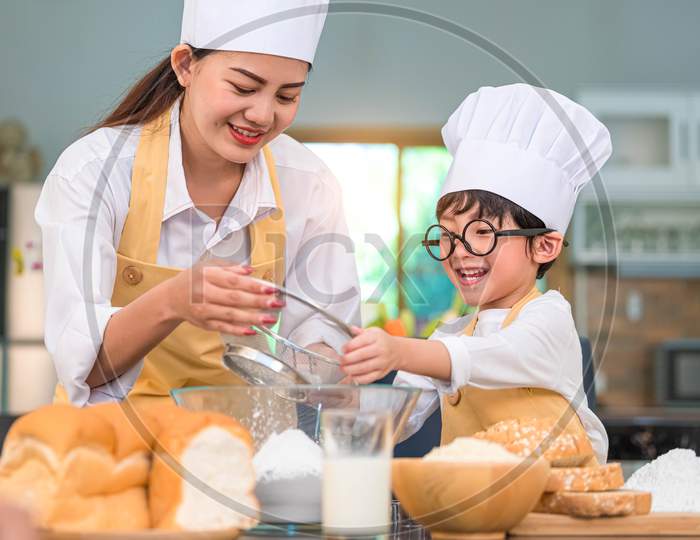Cute Little Asian Boy And Beautiful Mother Sifting Dough Flour With Sifter Sieve Colander In Home Kitchen On Table For Prepare To Baking Bakery And Cake. Thai Kids Playing With Flour As Chef Funny