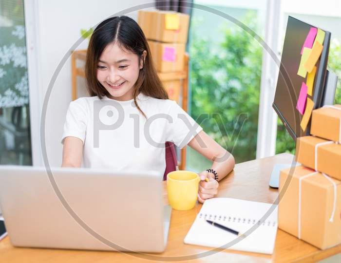 Asian Woman Enjoy Herself While Using  Internet On Laptop And Phone In Office. Business And Marketing And Part Time Concept. Online Shopping And Business Success Theme. Happy Mood Doing Working Job.