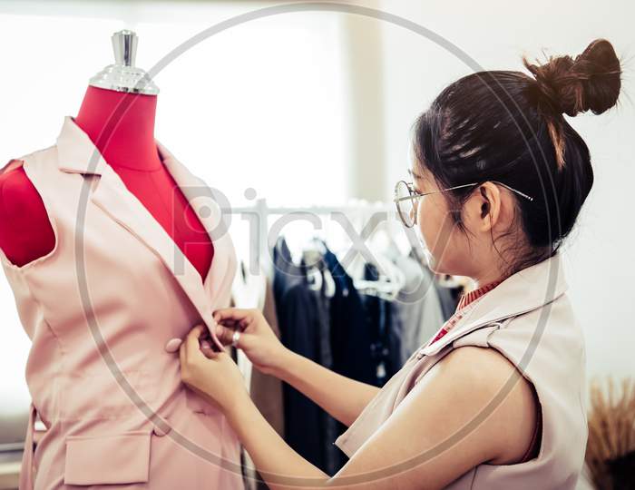 Asian Female Fashion Designer Girl Making Fit On The Formal Dress Uniform Clothes On Mannequin Model. Fashion Designer Stylish Showroom. Sewing And Tailor Concept. Creative Dressmaker Stylist.