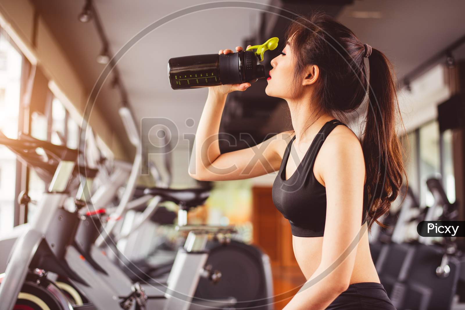 Asian Beautiful Woman Drinking Protein Shake Or Drinking Water In Sport Fitness Training Gym. Sports And People Concept. Fitness And Workout Theme. Girl Having Activity On Condominium Or Apartment