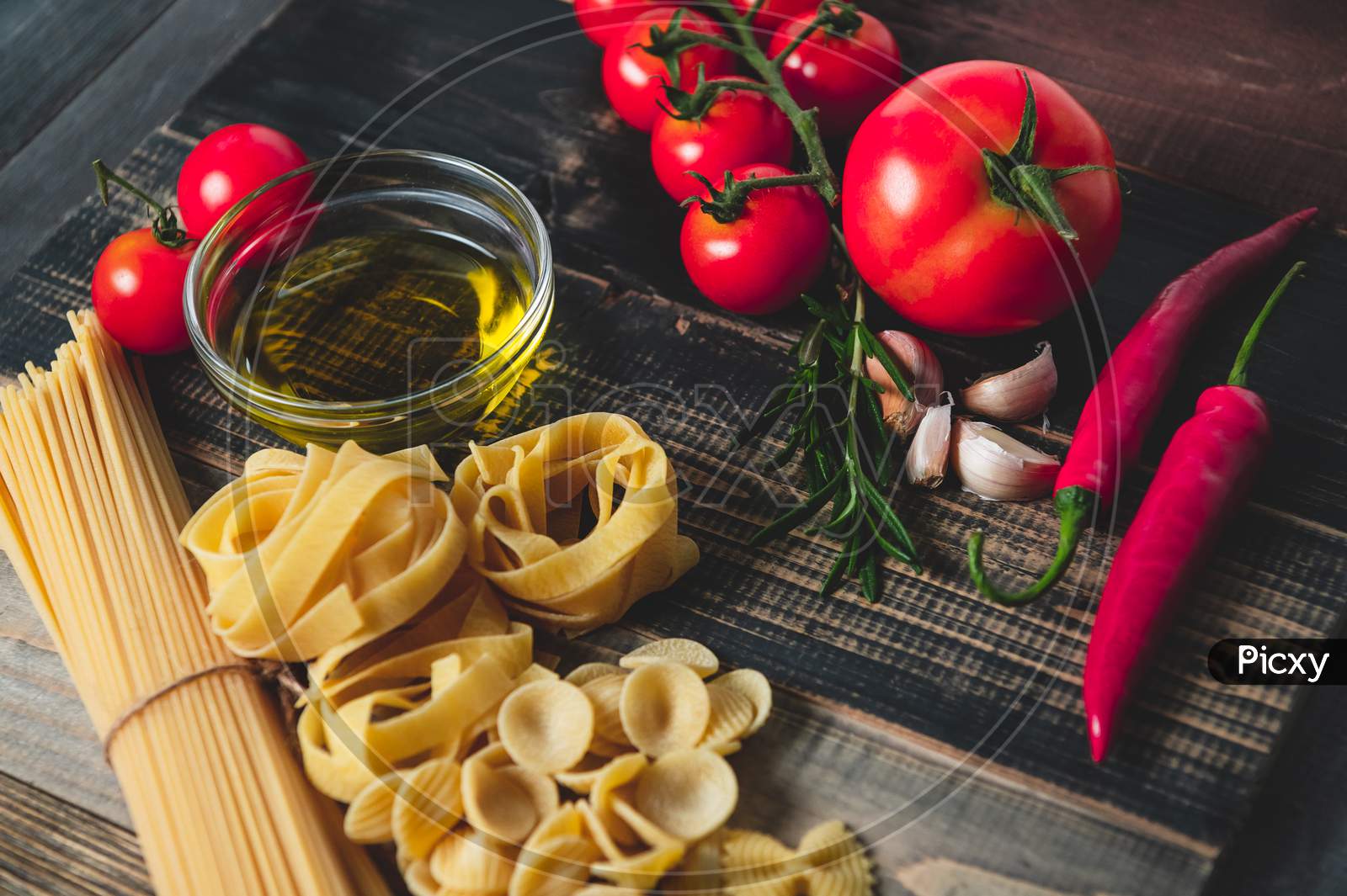 Tasty Appetizing Italian Spaghetti Pasta Ingredients For Kitchen Cuisine With Tomato, Cheese Parmesan, Olive Oil, Fettuccine And Basil On Wooden Brown Table. Food Italian Recipe Homemade. Top View