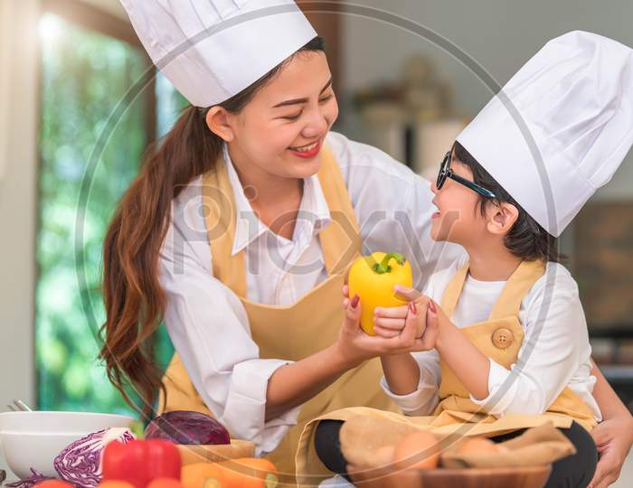 Happy Beautiful Asian Woman And Cute Little Boy With Eyeglasses Prepare To Cooking In Kitchen At Home. People Lifestyles And Family. Homemade Food And Ingredients Concept. Two Thai Looking Each Other