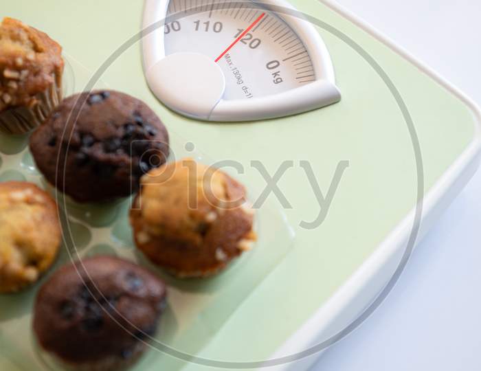 Closeup Of Weight Scale With Delicious  Fat And Sweet Bread Flavor On Top. Like Calories That Cause Weight Gain A Lot. Health And Beauty Concept. Diet And Healthcare. Overweight And Fitness
