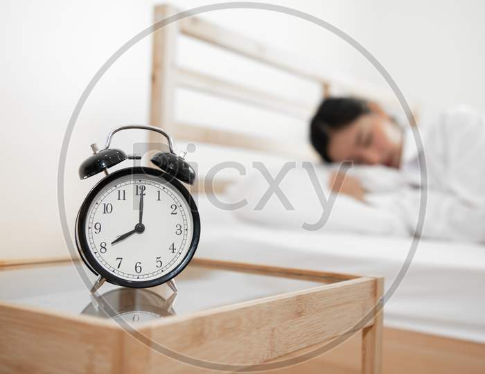 Closeup Alarm Clock With Sleeping Woman In Bed Room. Lazy Time In Holiday Concept.