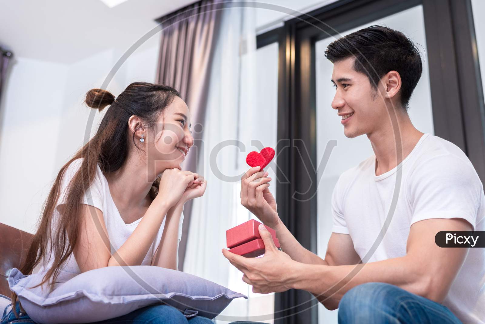 Man Holding Love Heart Symbol For Surprise Girlfriend At Their Home. Woman Waiting For Valentines Gift Form Boyfriend. Happy Birthday Party Anniversary Concept. People Couple Lifestyles And Family Life Theme