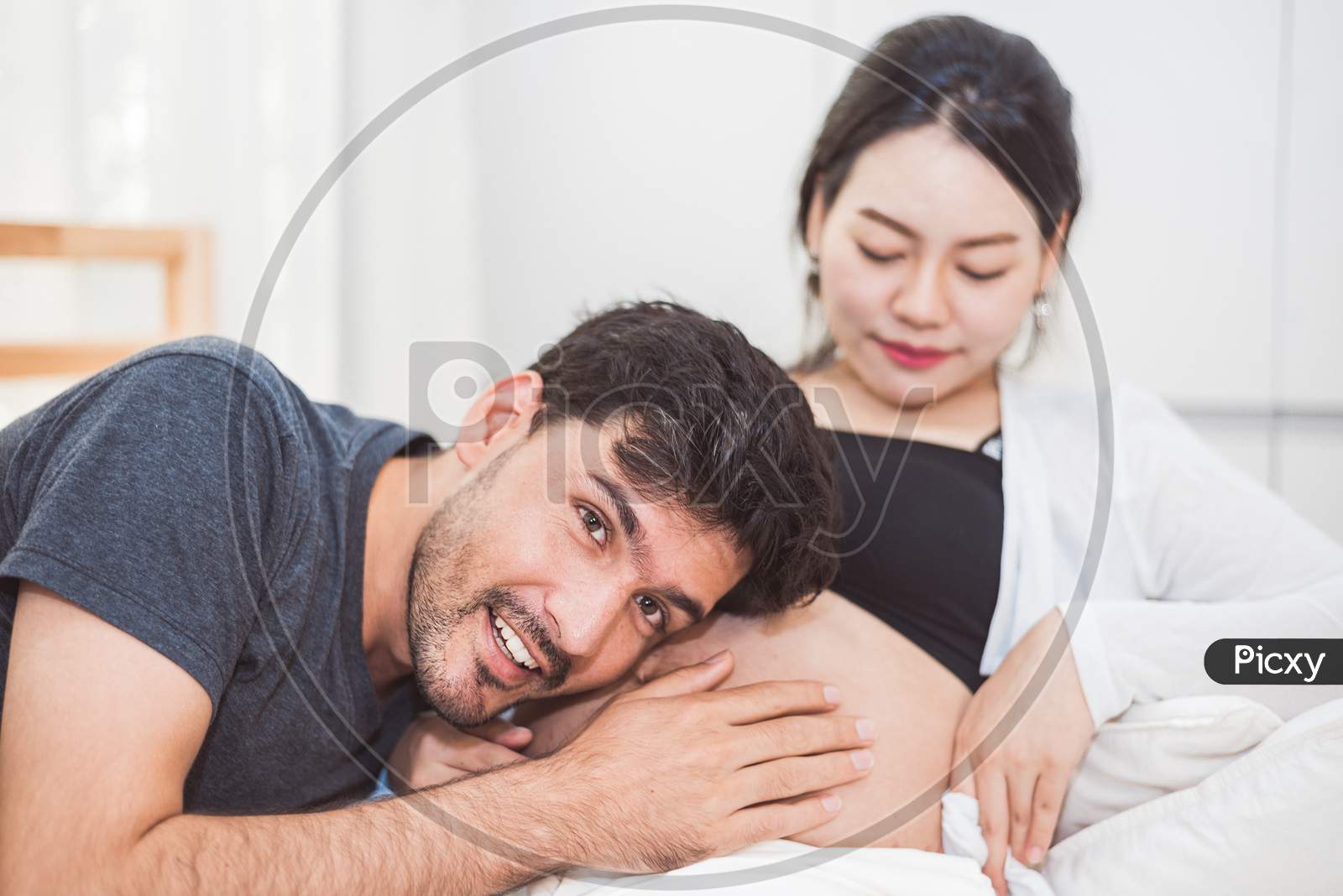 Father Hearing His Son Or Daughter Kicking Sound Check Inside Mother Belly When Sitting On Lying On Bed At Home. Family Healthy And Couples Concept. Happy Sweet Home Honeymoon And Wedding Theme