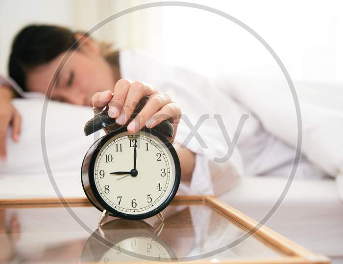Asian Young Beauty Woman Turning Off Alarm Clock In Morning Late Without Looking Clock And Lazy To Working On In Holiday. Bedroom And Bed Time Concept. Relaxation And People Lifestyles Of Tired Worker