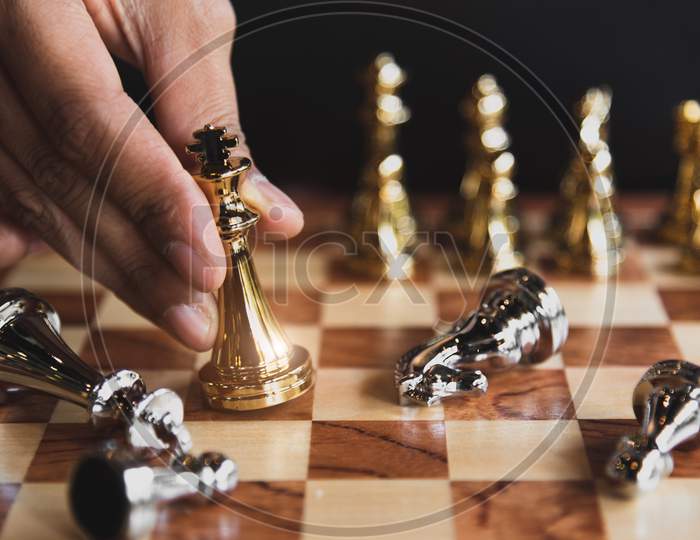 Hand Of Businessman Moving Golden Chess Figure For Eliminating In Battle Competition With Last Successful Ending Game. Leadership Strategy And Management Tactic Concept. Wooden Checkmate Chessboard
