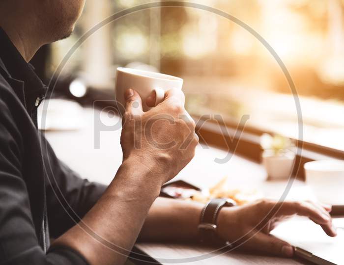 Close Up Of Coffee Cup On Businessman Hand. Man Working With Laptop Computer. Business And Technology Concept. Workaholics And Overnight Theme. Drinks And Relaxation Theme.