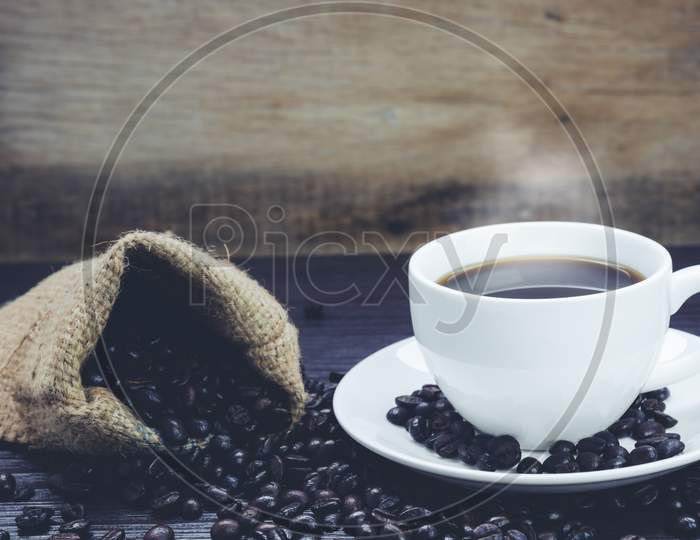 Side View Of Coffee Cup With  Smoke And Coffee Beans In Sack On Wood Table, Drinks And Relax Concept, For Advertising