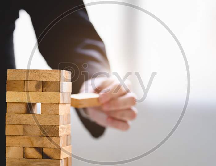 Businessman Take And Picking One Wood Block On Stacked Tower By Hand As Startup Project. Business Organization And Company Growth Progress. Success Of Strategy And Money Investment. Risk Management