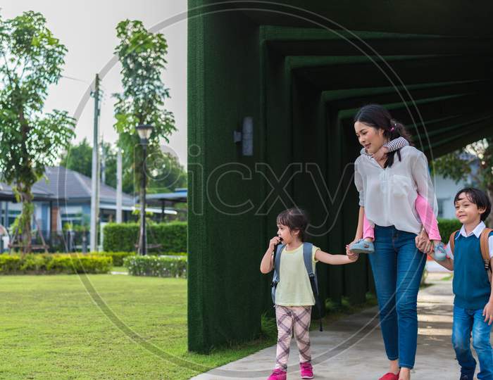 Single Mom Carrying And Playing With Her Children In Garden With Green Wall Background. People And Lifestyles Concept. Happy Family And Home Sweet Home Theme. Outdoors And Nature Theme.