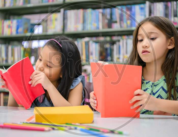 Two Little Cute Girls Multi-Ethnic Friends Reading Books Together In School Library. People Lifestyles And Education Learning Concept. Happy Friendship Kids Doing Leisure Activity For Examination Test