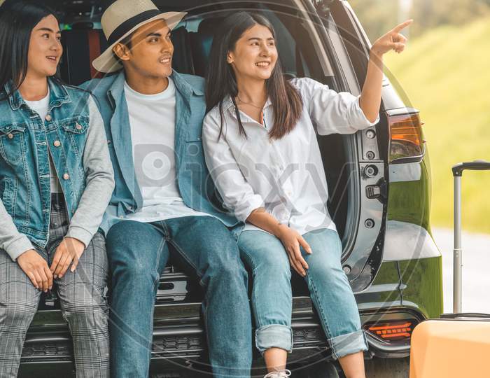 Asian Man And Women Relaxing In Back Of Car Trunk During Travel In Summer. Transportation And People Lifestyles Concept. Group Of Happy Friendship Sit And Looking Nature View. Relaxation In Vacation