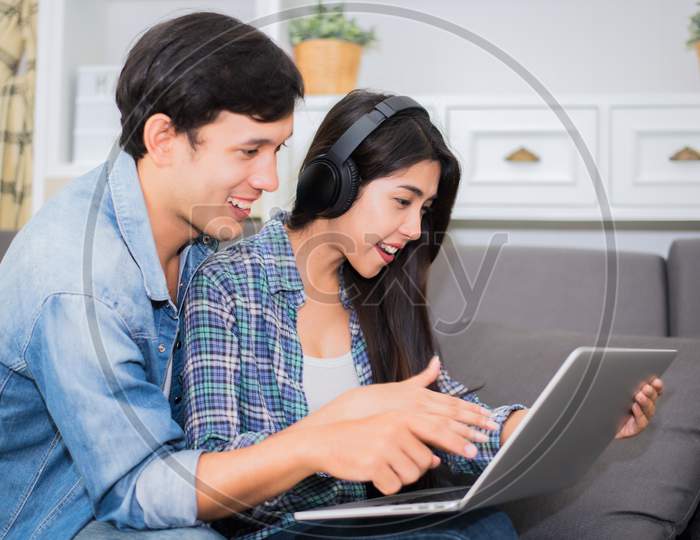 Lovers Or Couple Using Laptop And Listening Music With Headphone In House. Honeymoon And Entertainment Concept. Happiness And Lifestyle Concept. Communication Technology And People In Sweet Home Theme