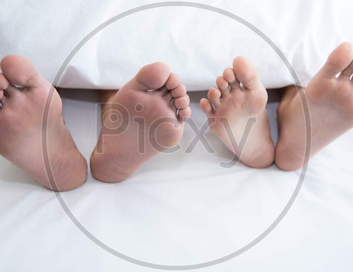 Close Up Of Couple Barefoot Under Blanket In Bedroom In Honeymoon Vacation Holiday In Long Weekend At Home. Relaxation Of Sexual And Romantic People After Wedding Ceremony. Valentines Day Love Theme.