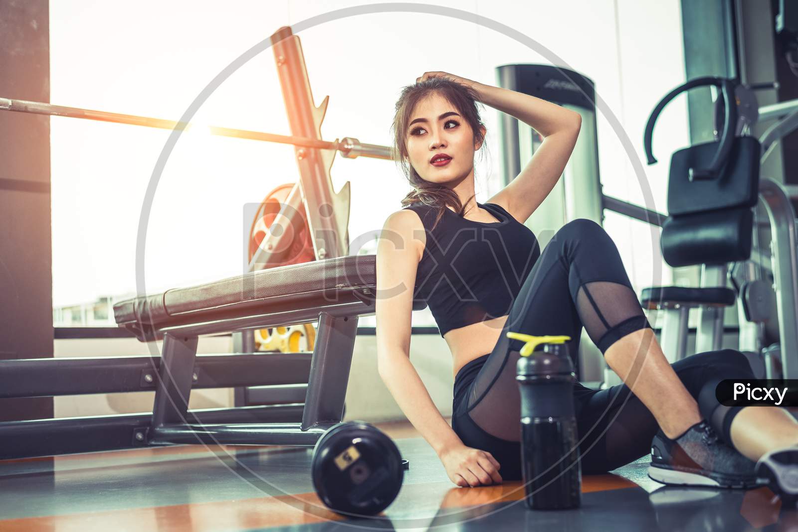 Asian Young Woman Relaxing In Fitness Gym And Sport Club Center With Equipment And Dumbbell. Workout And Strength Training Concept. Beauty And Healthy Theme. Gymnasium Background