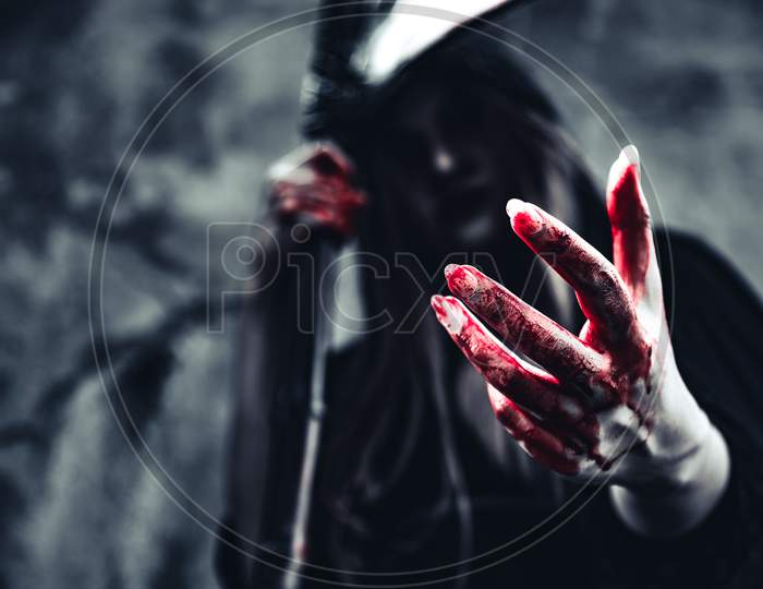 Witch Showing Bloody Hand. Female Demon Angel In Black Clothes And Hood On Grunge Wall Background. Halloween Day And Mystery Concept. Fantasy Of Magic Theme. Afterlife And Death Concept.