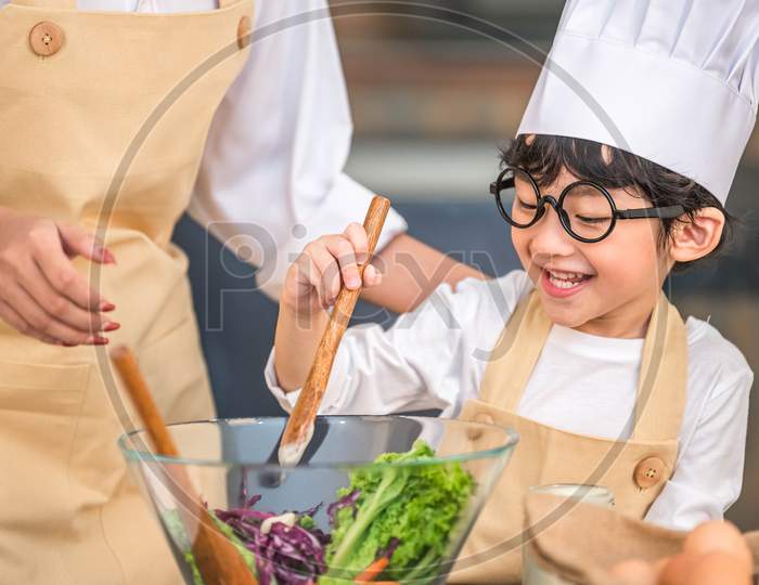 Cute Little Asian Happy Boy Interested In Cooking With Mother Funny In Home Kitchen. People Lifestyles And Family. Homemade Food And Ingredients Concept. Two Thai People Making Ketogenic Diet Salad