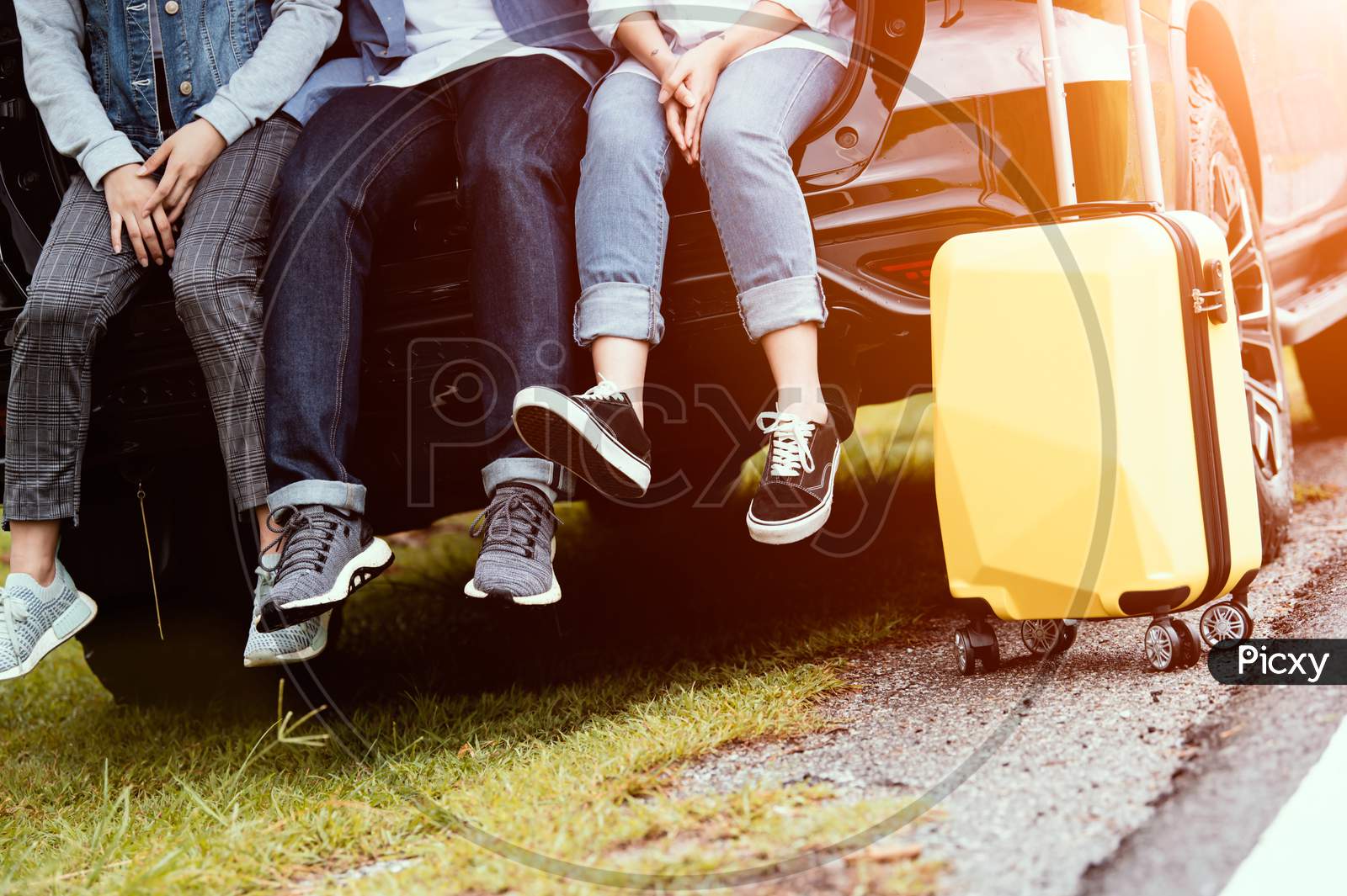 Closeup Lower Body Of Group Of Friends Relaxing On Suv Car Trunk With Trolly Luggage Along Road Trip With Autumn Mountain Hill Background. Freedom  Road Way. People Lifestyle Transportation Travel