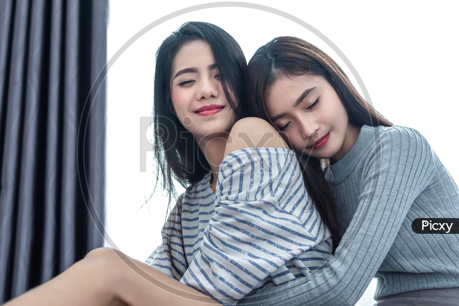 Two Asian Lesbian Women Hug Together In Bedroom. Couple People And Beauty Concept. Happy Lifestyle And Home Sweet Home Theme. Cushion Pillow Element And Window Curtain Background. Love Scene Of Lovers
