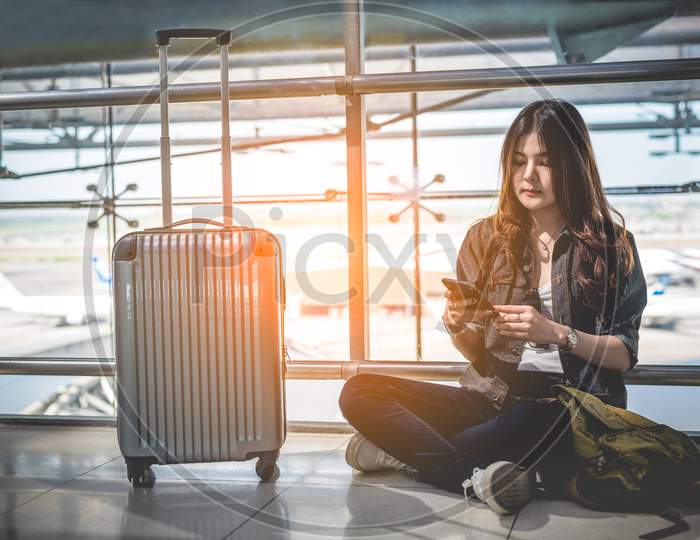 Asian Female Traveler Using Smart Phone For Checking Flight Time Schedule At Airport. People And Lifestyles Concept. Technology And Business Concept.