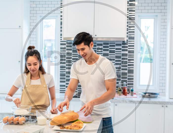 Happy Asian Couples Cooking And Baking Cake Together In Kitchen Room. Man And Woman Looking To Tablet Follow Recipe Step At Home. Love And Happiness Concept. Sweet Honeymoon And Valentine Day Theme