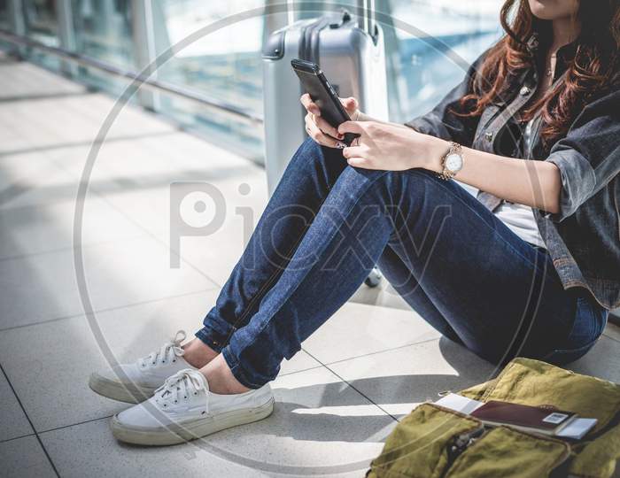 Close Up Of Young Woman With Bag And Suitcase Luggage Waiting For Departure While Sitting In Airport Lounge. Female Traveler And Tourist Theme. High Season And Vacation Concept. Relax And Lifestyles