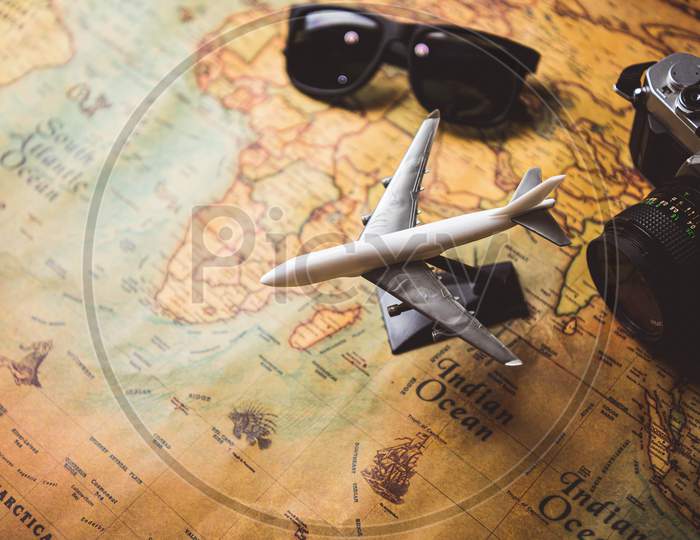 Tourist Planning Props And Travel Accessories With Airplane, Digital Camera And Sunglasses On Old Grunge Style Map Desktop. Holiday Destination And Vacation Concept. Copyspace