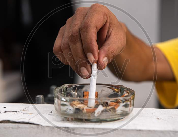 Hand Putting Out Cigarette And Destroy In Ashtray At Outdoor In Front Of House. Healthy And People Concept. World No Tobacco Day Theme