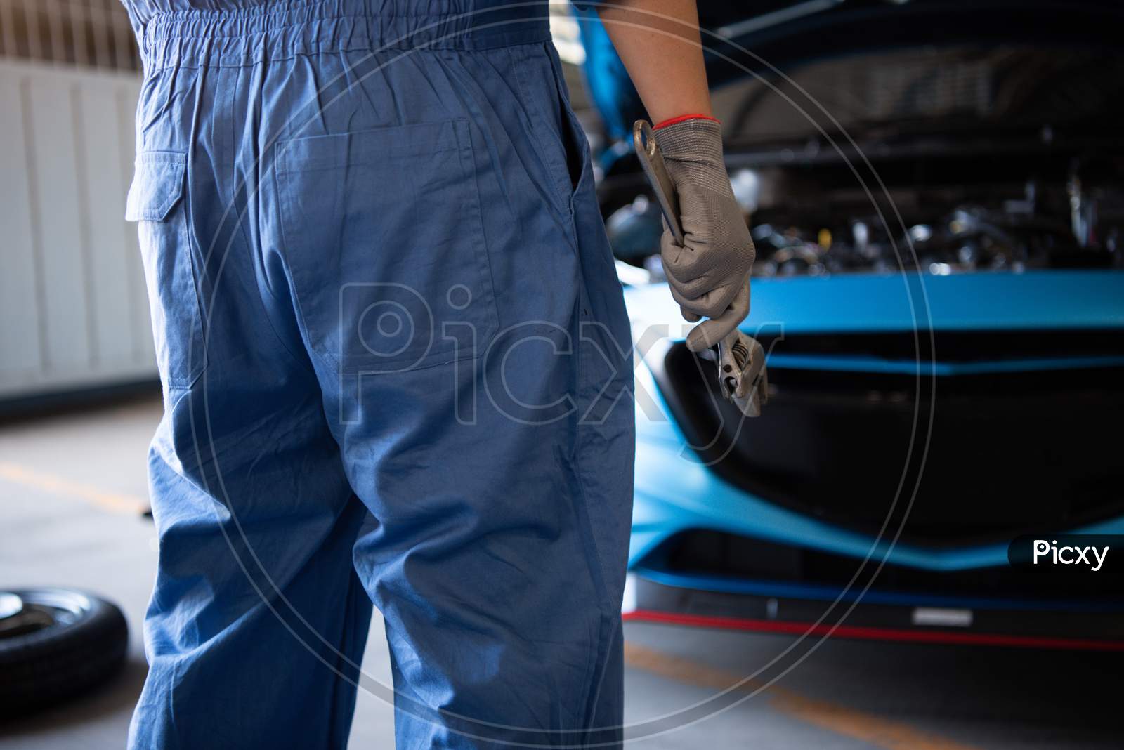 Car Mechanic Holding Wrench For Fixing To Customer Claim Order In A Auto Repair Garage Workshop. Engine Repair Service. People Occupation And Business Job. Automobile Industry Technical Maintenance