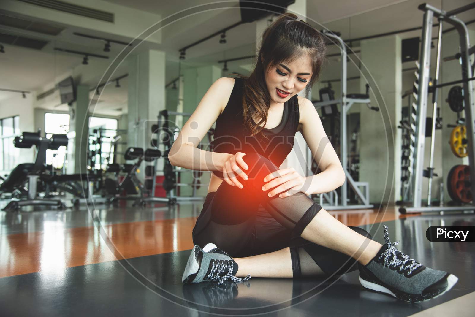 Asian Woman Injuries During Workout At Knee In Fitness Gym Sport Center. Medical And Healthcare Concept. Exercise And Training Theme. People Healthy Lifestyle And Leisure Activity Problem