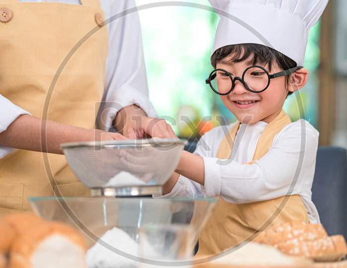 Cute Little Asian Boy And Beautiful Mother Sifting Dough Flour With Sifter Sieve Colander In Home Kitchen On Table For Prepare To Baking Bakery And Cake. Thai Kids Playing With Flour As Chef Funny