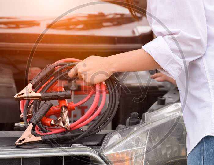 Closeup Of Woman Hand Holding Battery Cable Copper Wire For Repairing Broken Car By Connect Battery With Red And Black Line To Electric Terminal By Herself. Car Maintenance And Transportation Concept