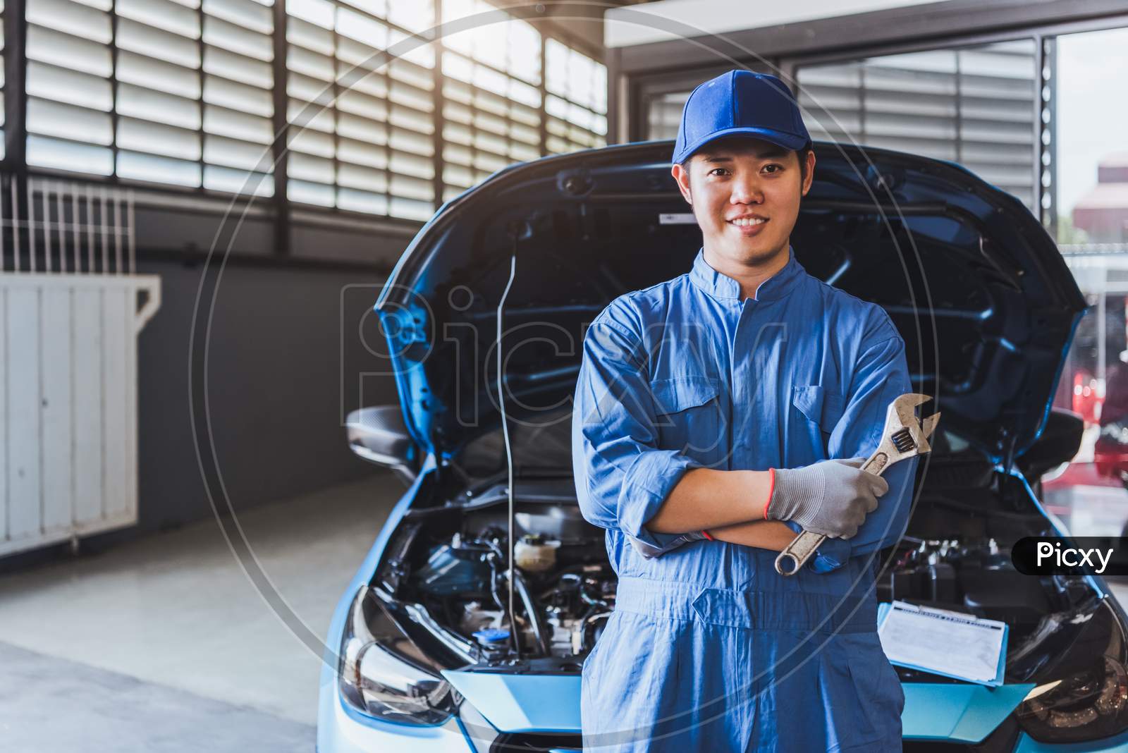 Happy Car Mechanic Inspection Technician Holding Wrench And Smiling To Camera After Fixing Customer Car Claim In Service Maintenance Insurance Of Car Engine. Transportation Automotive Industry Concept